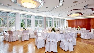 A banquet hall with round tables set for a formal event, large windows, and a wooden floor.