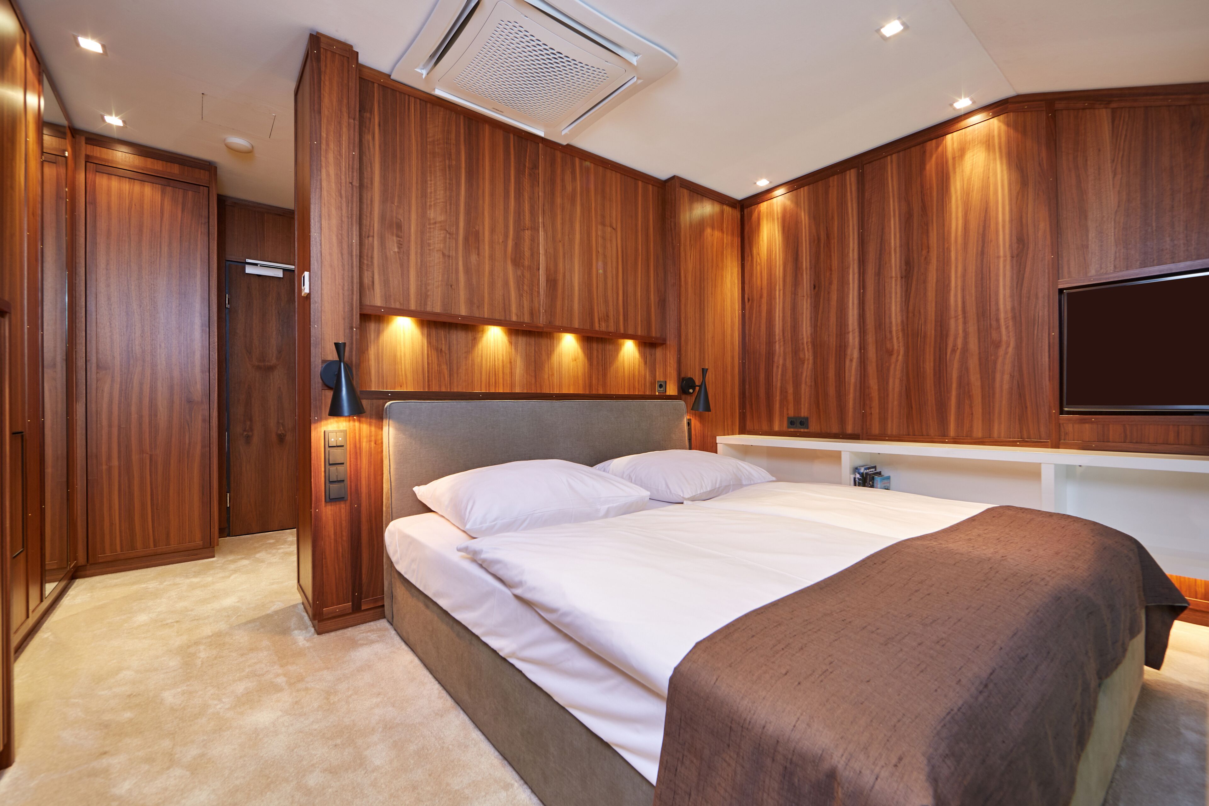 Ein modernes Schlafzimmer mit Holzvertäfelung, einem großen Bett, einem Flachbildfernseher und einer integrierten Klimaanlage.