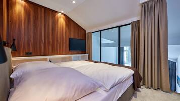 A modern hotel room with a large bed, a flat-screen TV mounted on the wall, and a large window with curtains.