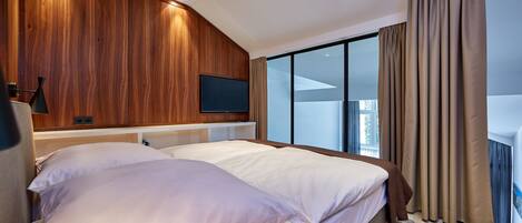Ein modernes Hotelzimmer mit einem großen Bett, einem flachbildfernseher an der Wand und einem großen Fenster mit Vorhängen.