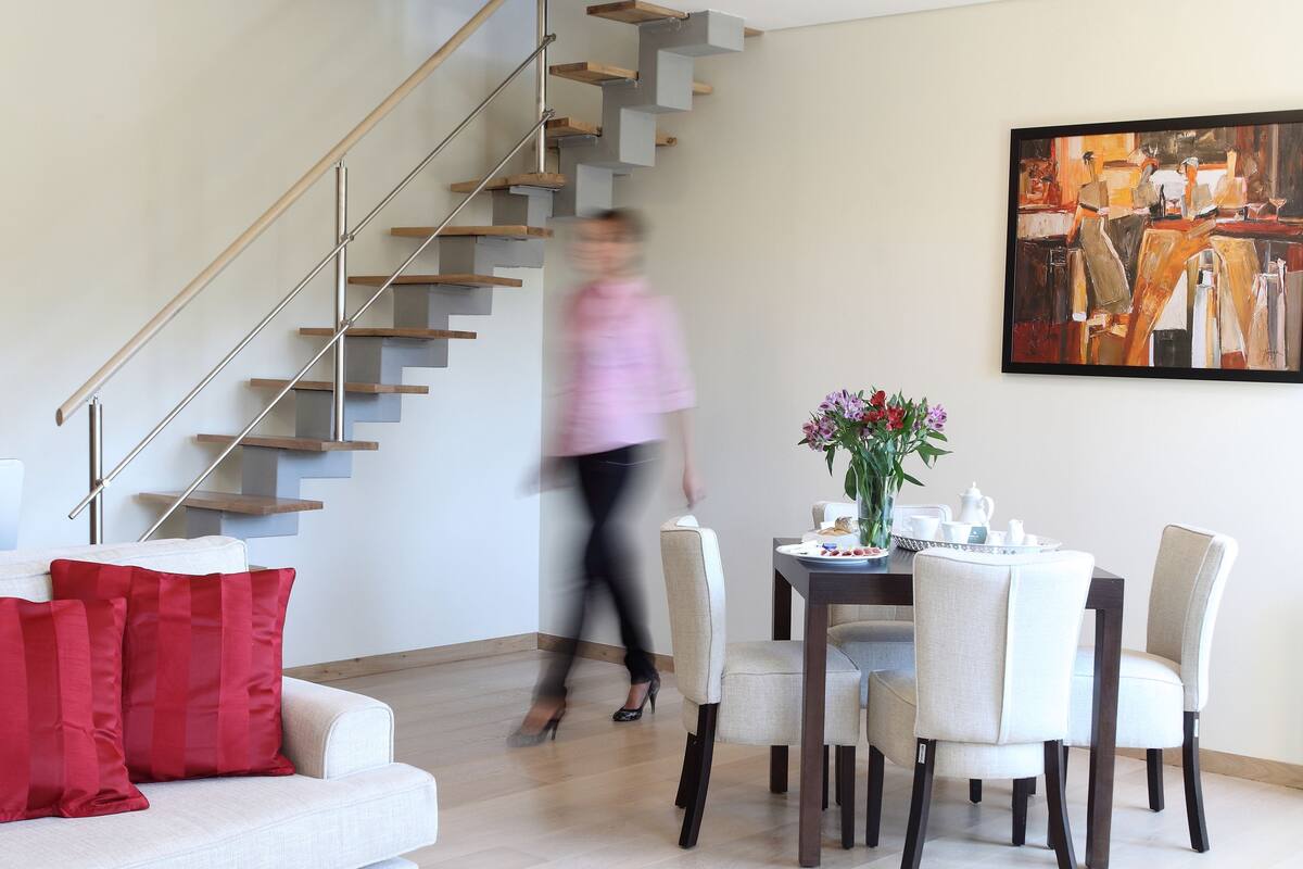 A modern living room with a staircase, a dining area, and a coffee table with fruits.
