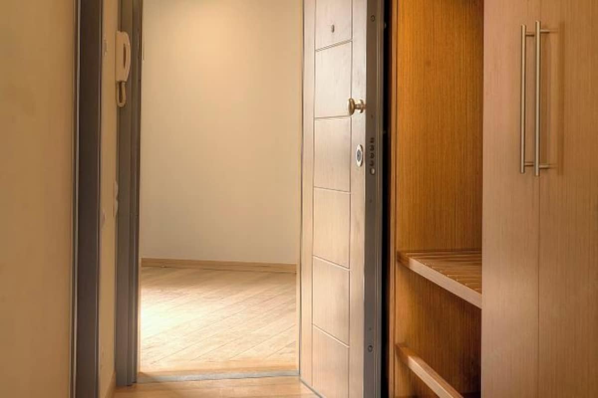 A hallway with a wooden floor leading to a room with a wooden wardrobe and a door with a handle.