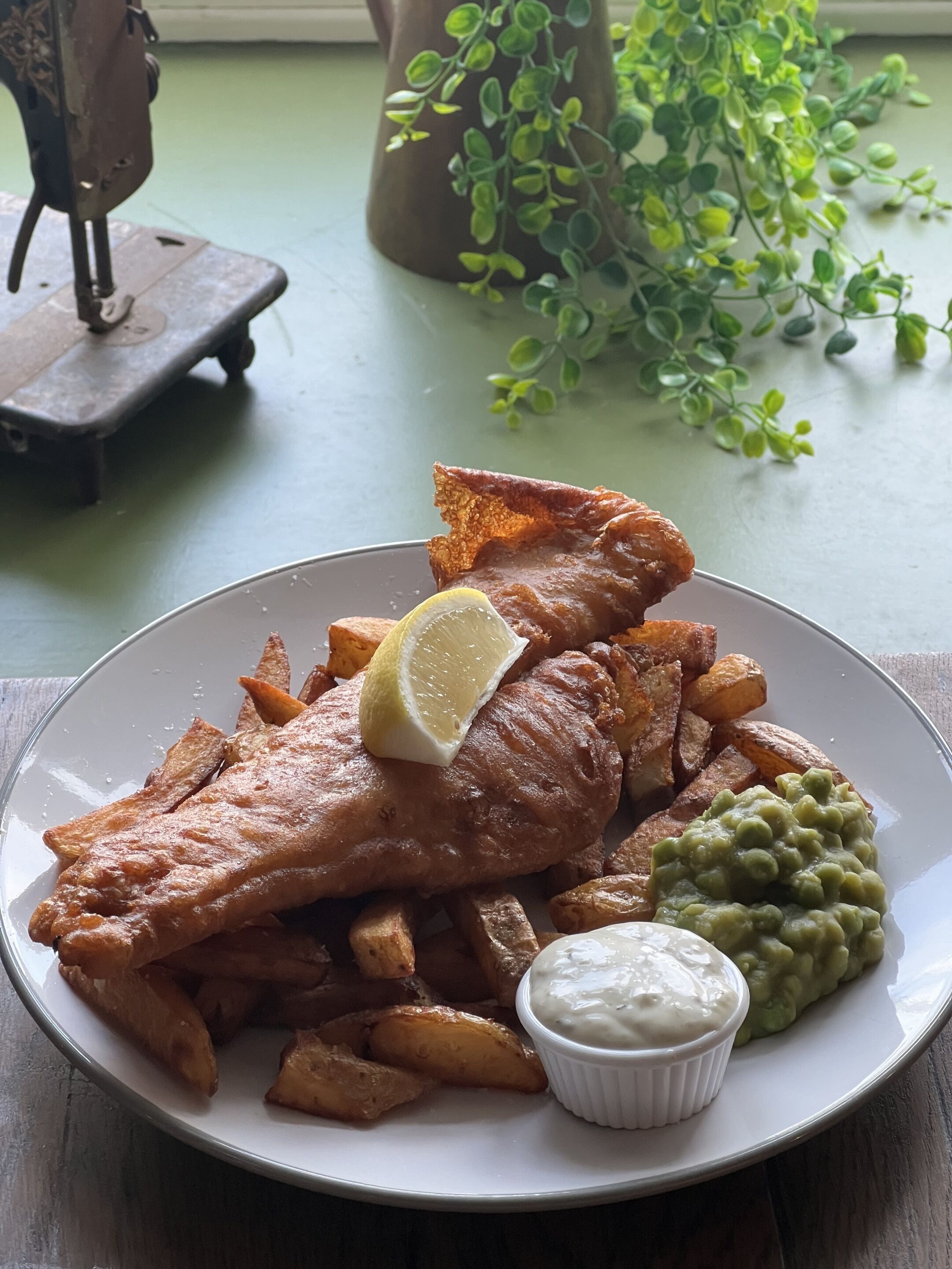 Een bord vis en friet met een partje citroen, frieten en mushy peas.