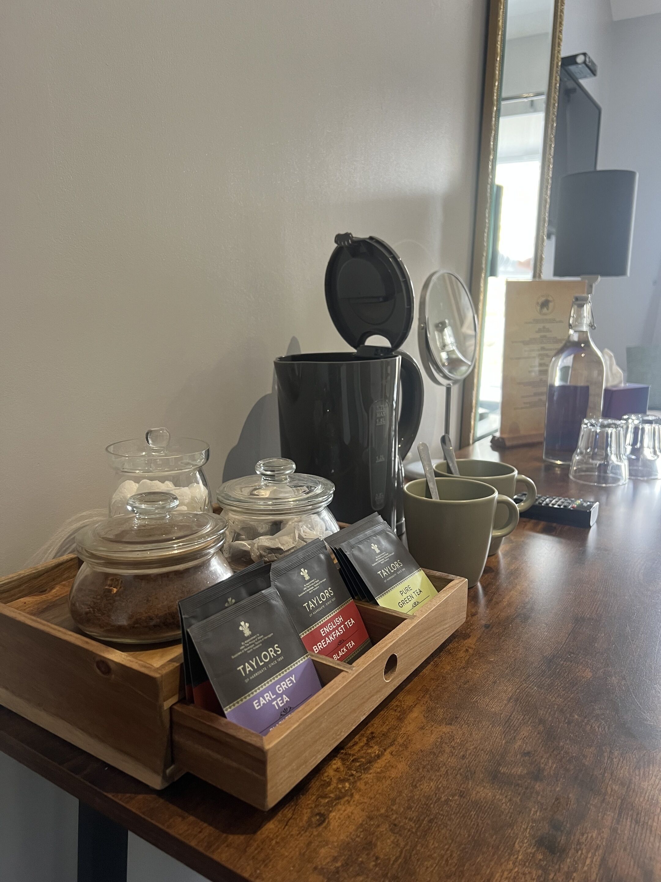 A wooden tray with tea packets, a glass jar, and a black container on a wooden table.