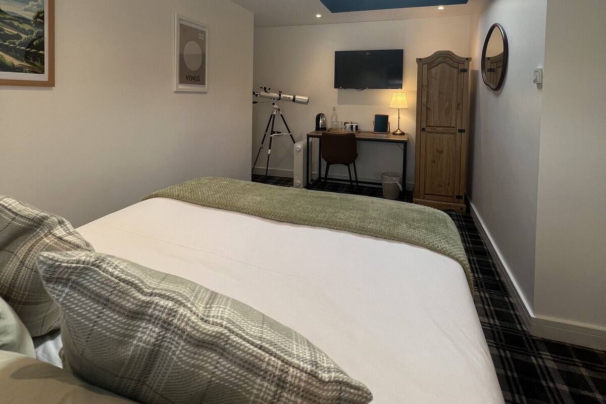Una camera da letto con un velux, un letto con cuscini verdi, una scrivania con un computer e un televisore a parete.
