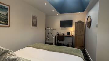 A bedroom with a skylight, a bed with green pillows, a desk with a computer, and a mounted TV.