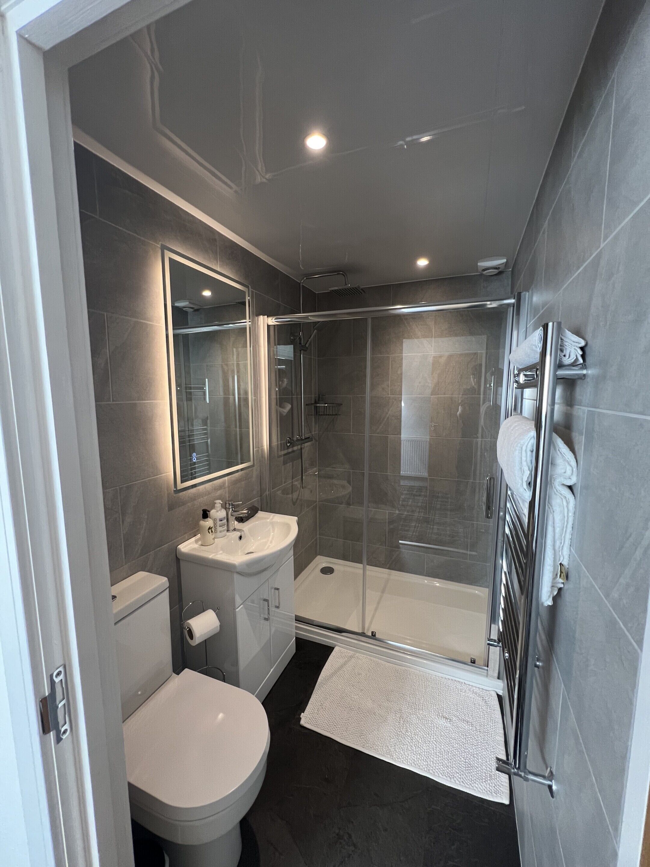 Un baño moderno con cabina de ducha de vidrio, inodoro y lavabo con espejo.