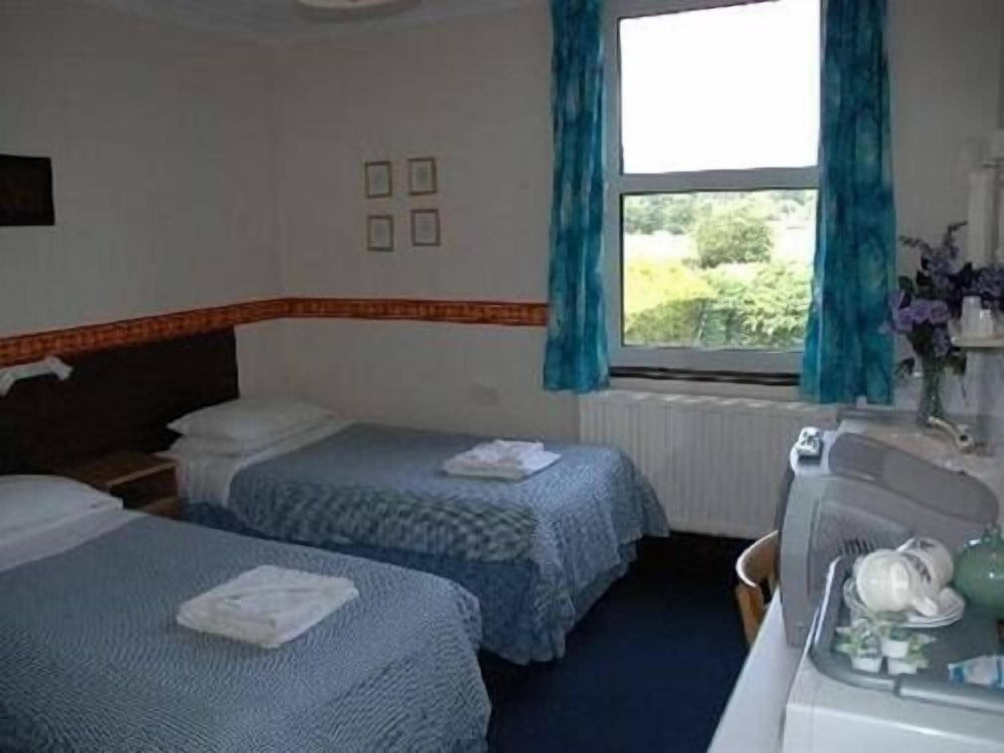 Une chambre d’hôtel avec deux lits, un bureau avec une chaise, une fenêtre avec des rideaux et un radiateur.