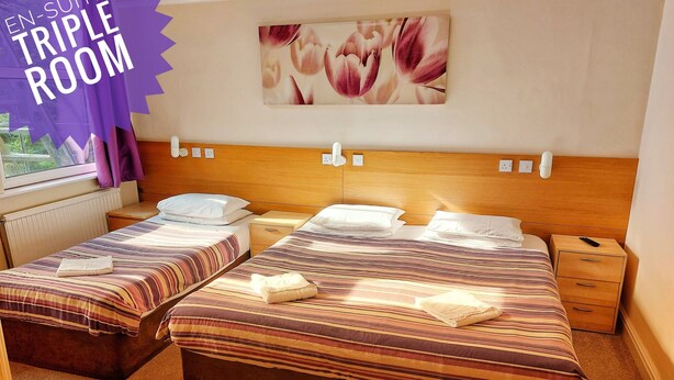 Habitación de hotel con dos camas, cabecero de madera, ventana con cortinas e imagen colgada en la pared.