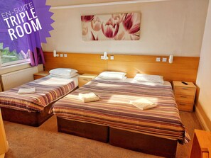 A hotel room with two beds, a wooden headboard, a window with curtains, and a wall-mounted picture. - Bridge Guest House (Ipswich)