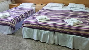 Una habitación de hotel con dos camas individuales, cada una con colcha a rayas y almohadas blancas. Hay mesitas de noche de madera con cajones y una pequeña mesa entre las camas.