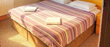 A double room with a wooden headboard, striped bedding, and three wall-mounted rose paintings.
