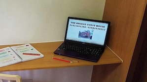 Un ordenador portátil sobre un escritorio, junto con un cuaderno y un lápiz, una silla de madera y un suelo alfombrado.
