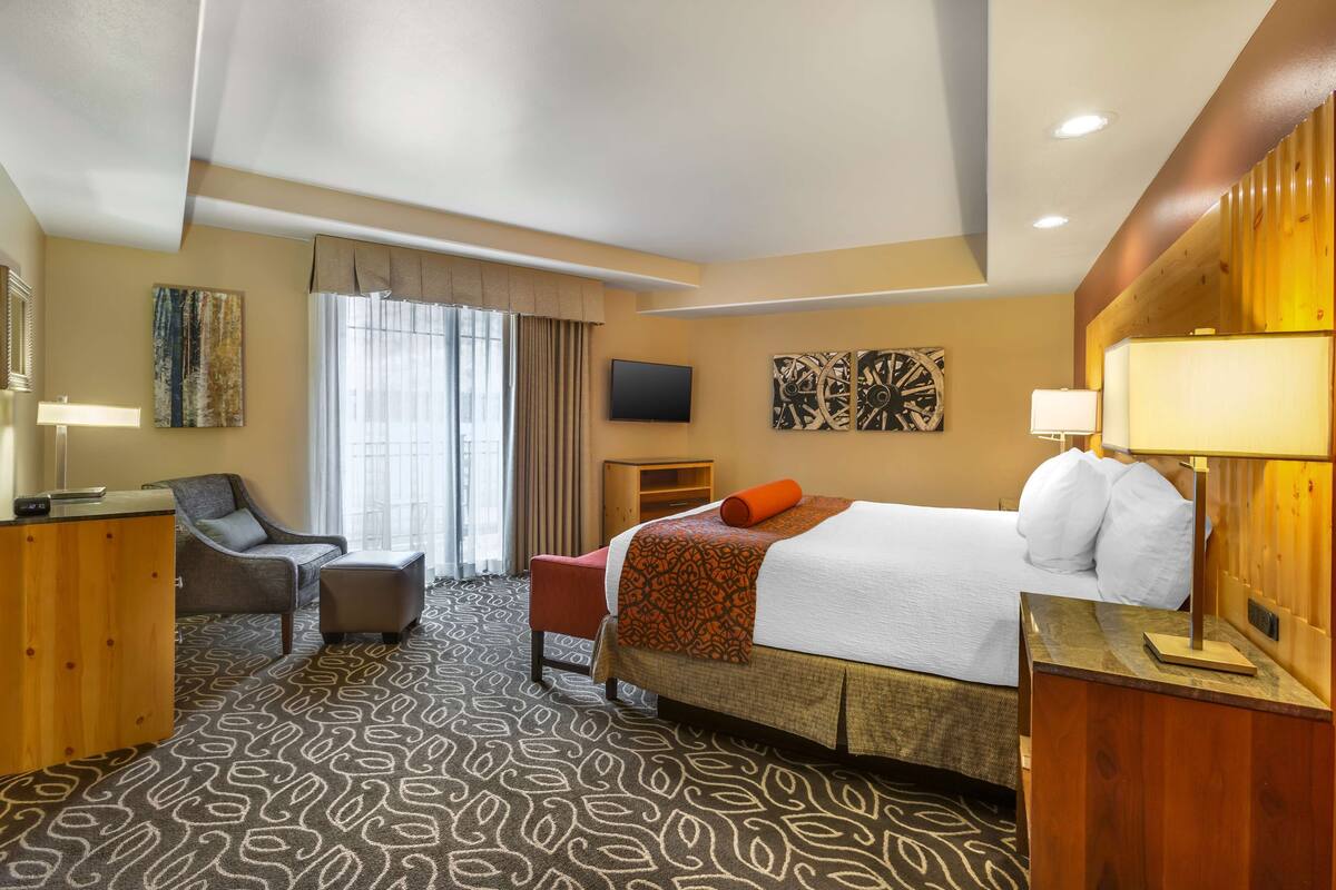A hotel room with a bed, a desk, a chair, a TV, and artwork on the walls.