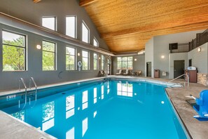 An indoor swimming pool with clear windows, a wooden ceiling, and a view of trees outside.