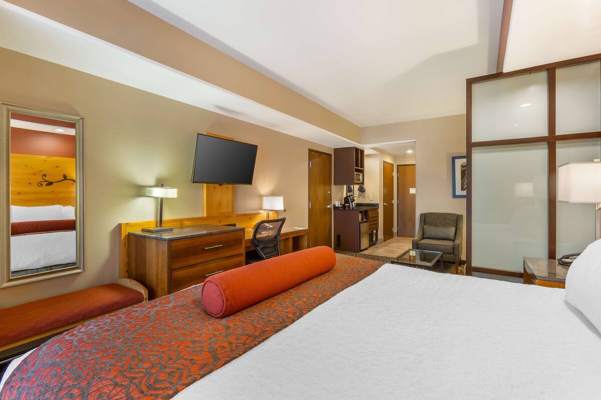 A hotel room with a large bed, a desk, a chair, a TV, and a bathroom visible through an open door.