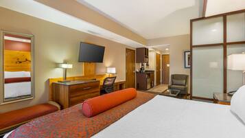 A hotel room with a large bed, a desk, a chair, a TV, and a bathroom visible through an open door.