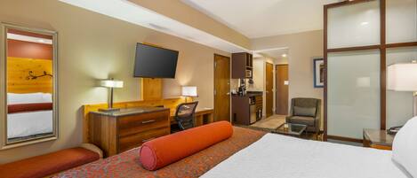 A hotel room with a large bed, a desk, a chair, a TV, and a bathroom visible through an open door.