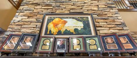 A stone wall with a framed buffalo mural and several framed awards on a shelf.
