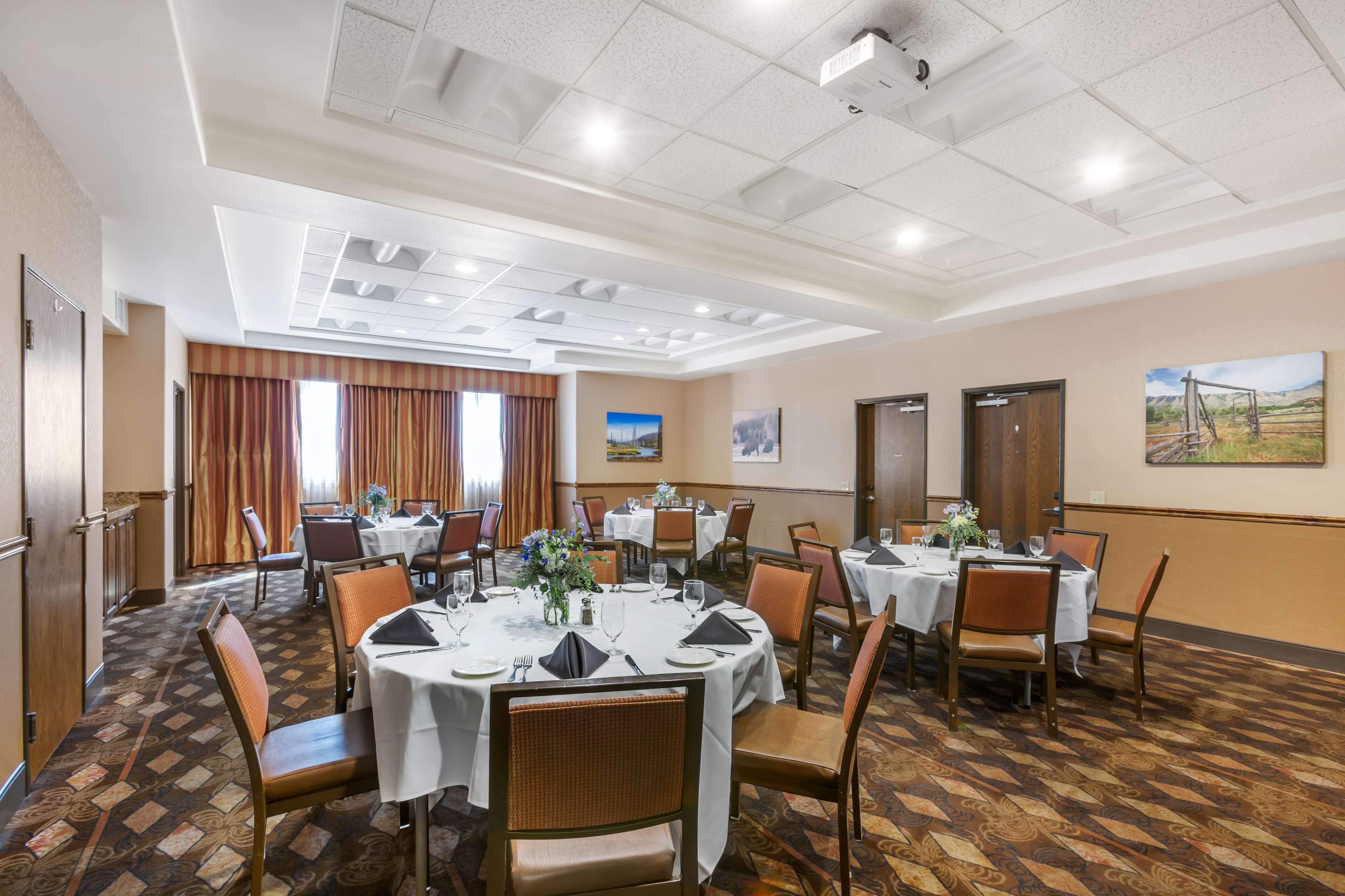 A hotel dining area with multiple round tables, chairs, and a patterned carpet.