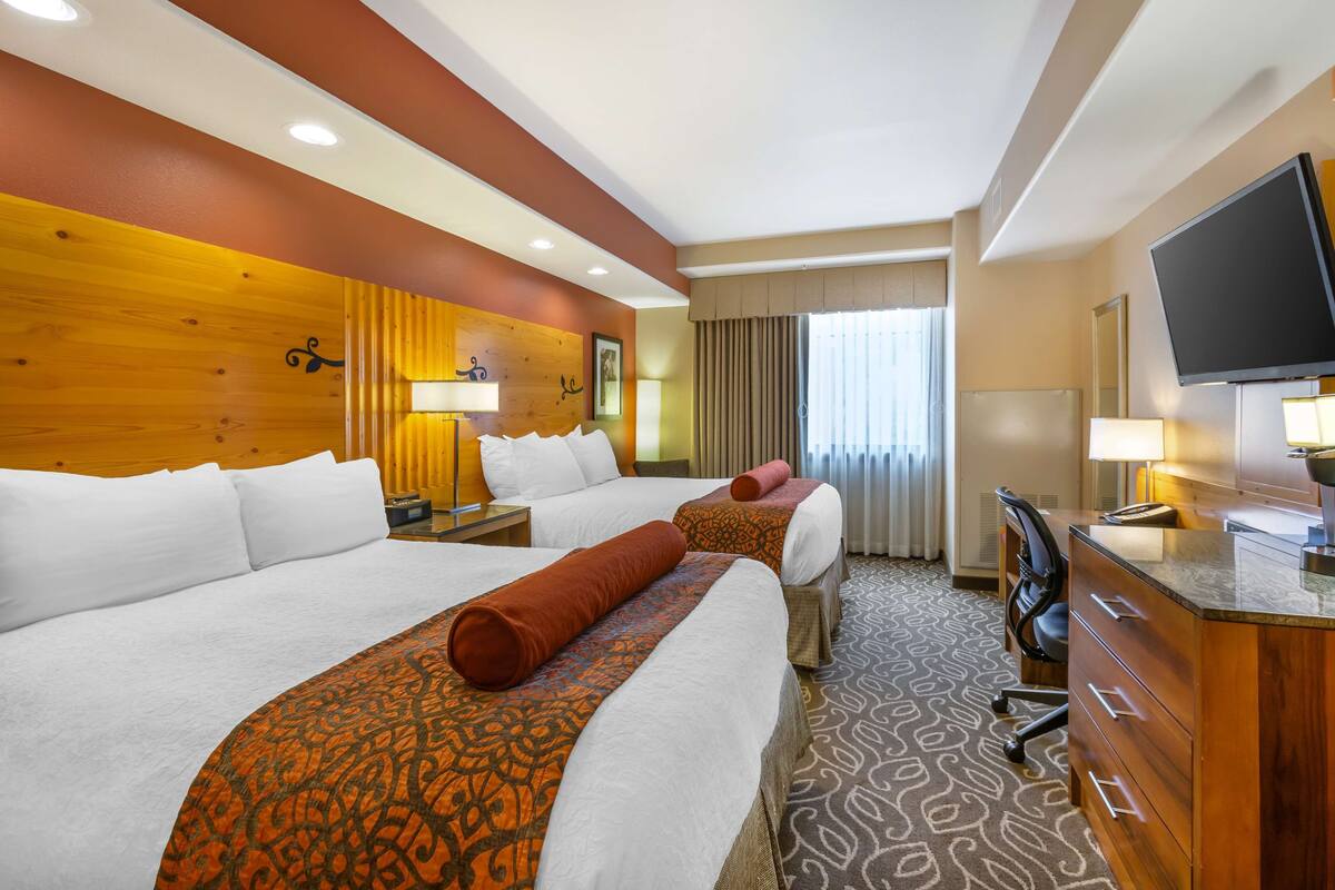 A hotel room with two beds, a desk, a television, and a bathroom.