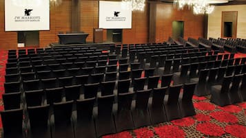 Un salón de conferencias con filas de sillas negras, un atril y una pantalla grande que muestra el logotipo de JW Marriott.