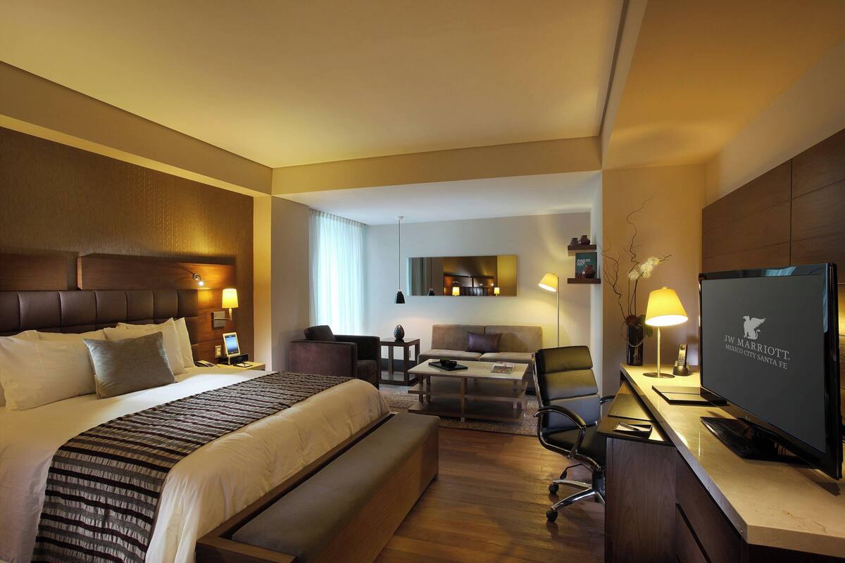 Une chambre d’hôtel avec un grand lit, un bureau avec une télévision, un canapé et une petite table avec une lampe.