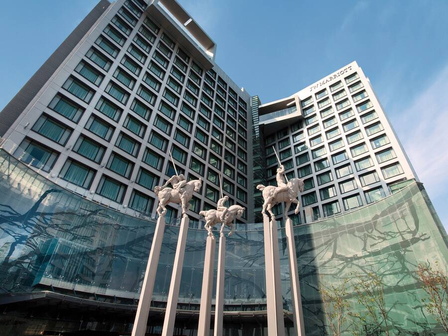 A modern hotel with a glass facade and a distinctive sculpture of riders on horses.