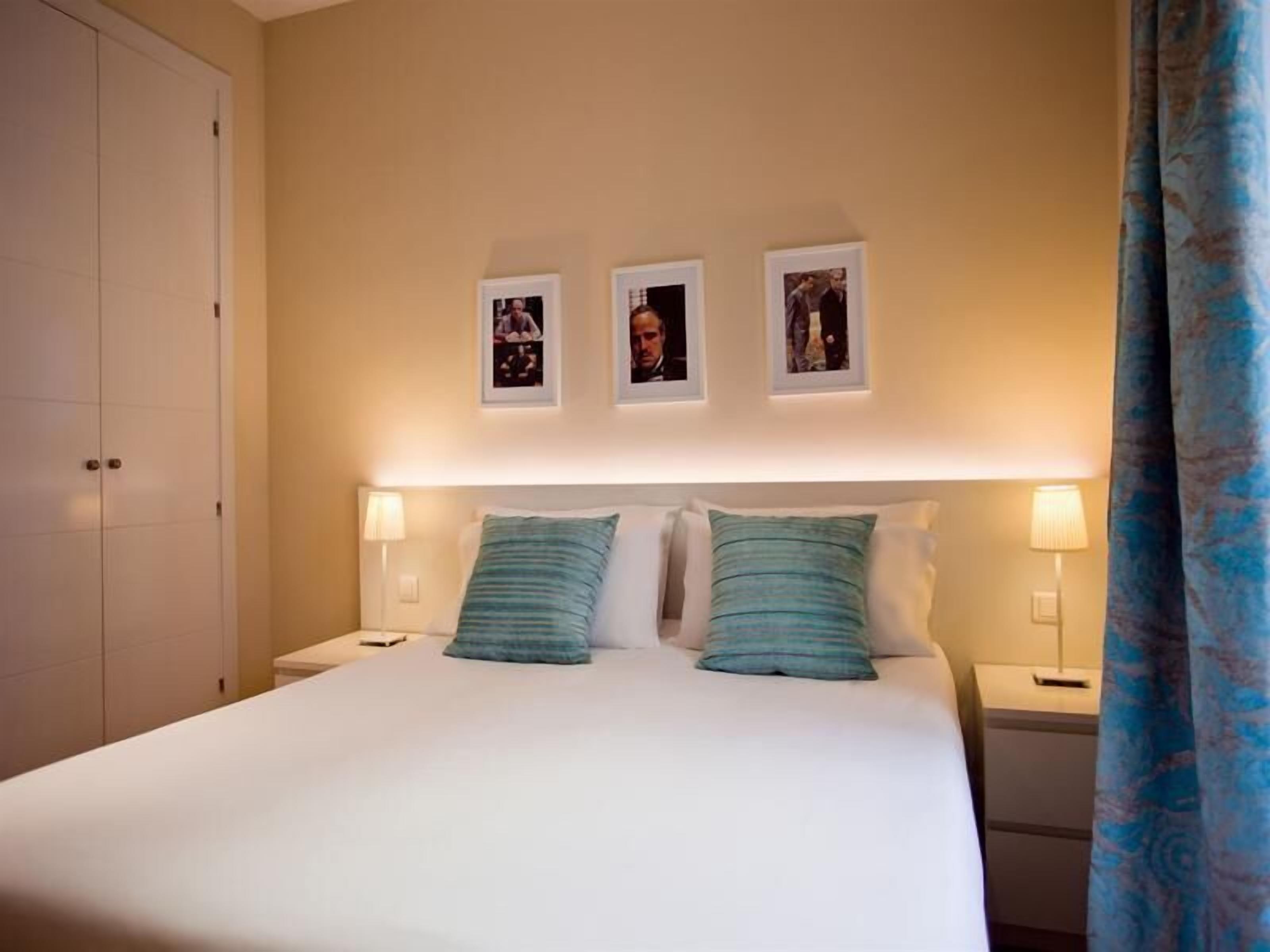 A hotel room with a bed, two bedside lamps, and three framed pictures on the wall.