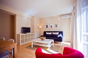 A modern living room with a white coffee table, a dark blue sofa with striped pillows, a flat-screen TV on a white stand, and a basket on the table. - Apartment in the Centre (Madrid)