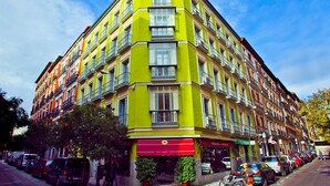 Un edificio de varios pisos con entrada en esquina, varios balcones y un toldo rojo.