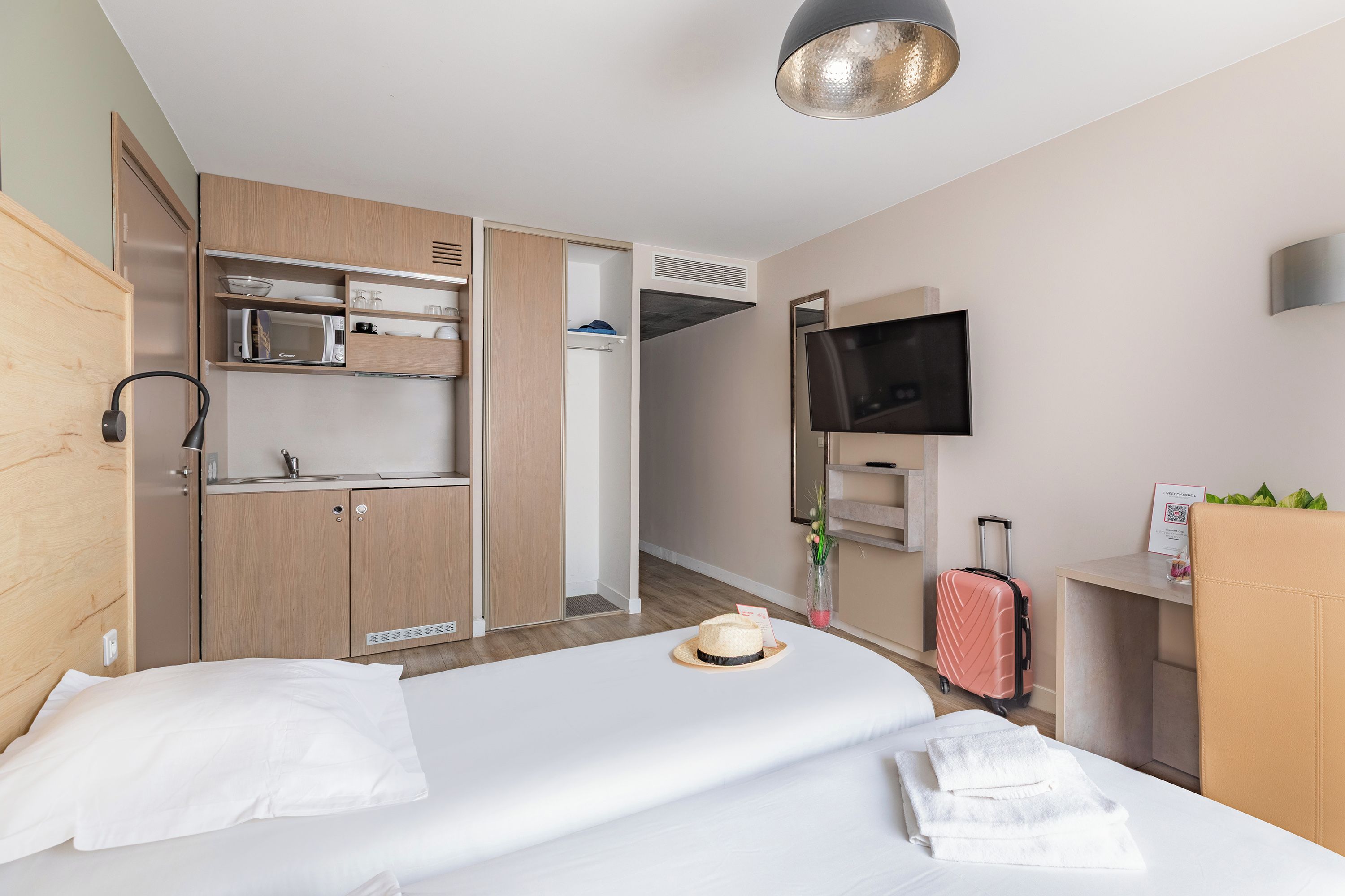 Quarto de hotel com cama, televisão, escrivaninha, guarda-roupa e banheiro.