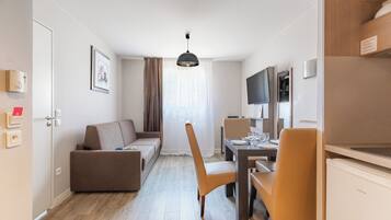 Une pièce moderne et bien éclairée, avec un canapé, une table à manger et des chaises. On y trouve également un téléviseur et un réfrigérateur.
