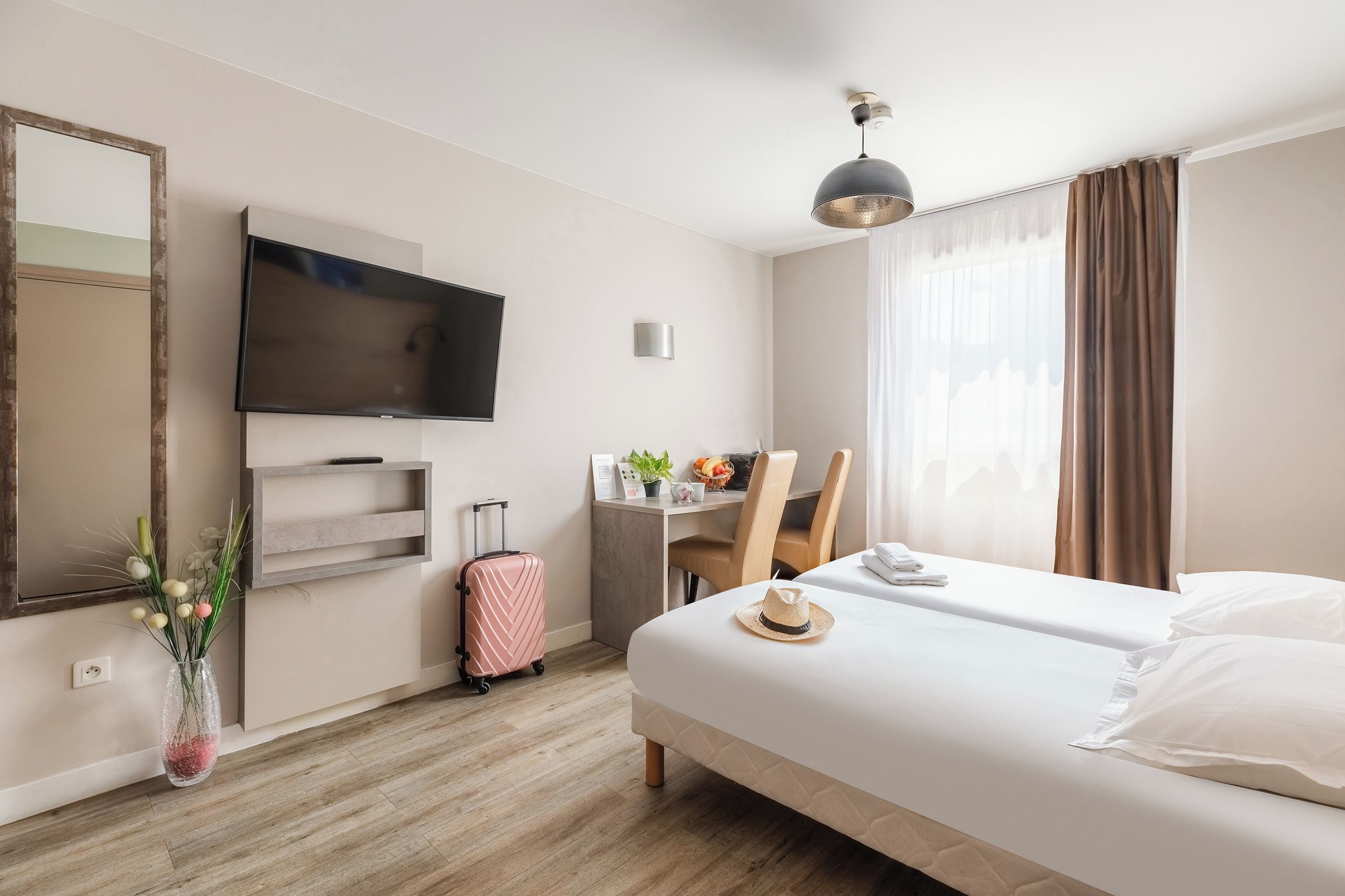 A hotel room with a bed, a desk, a television, a mirror, and a window with curtains.
