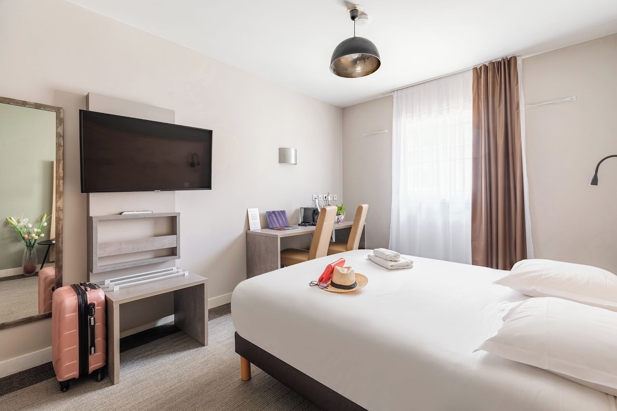 Una habitación de hotel con una cama, un escritorio, un televisor y una maleta.