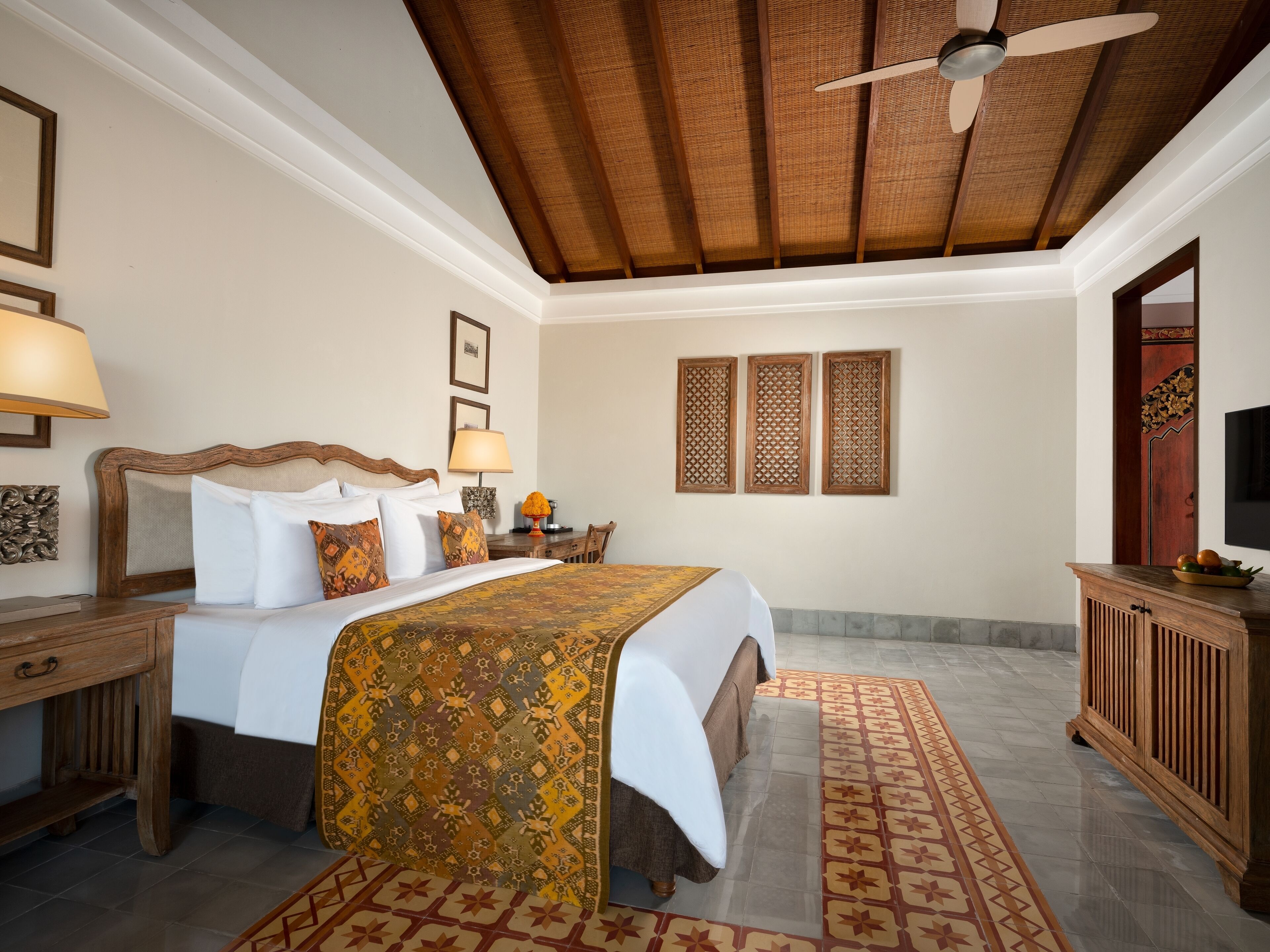 Habitación de hotel con cama, mesita de noche, escritorio, silla, televisor y ventilador de techo.