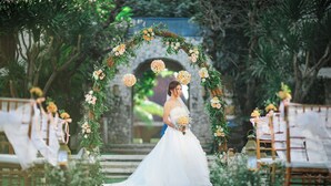 Une cérémonie de mariage où la mariée, vêtue d’une robe blanche, se tient sous une arche décorée de fleurs.