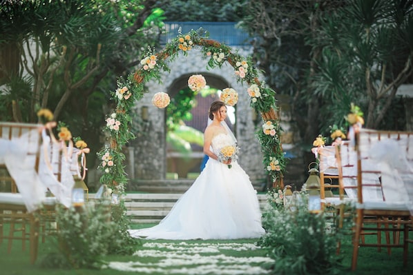 Una ceremonia de boda con una novia en vestido blanco, de pie bajo un arco floral.