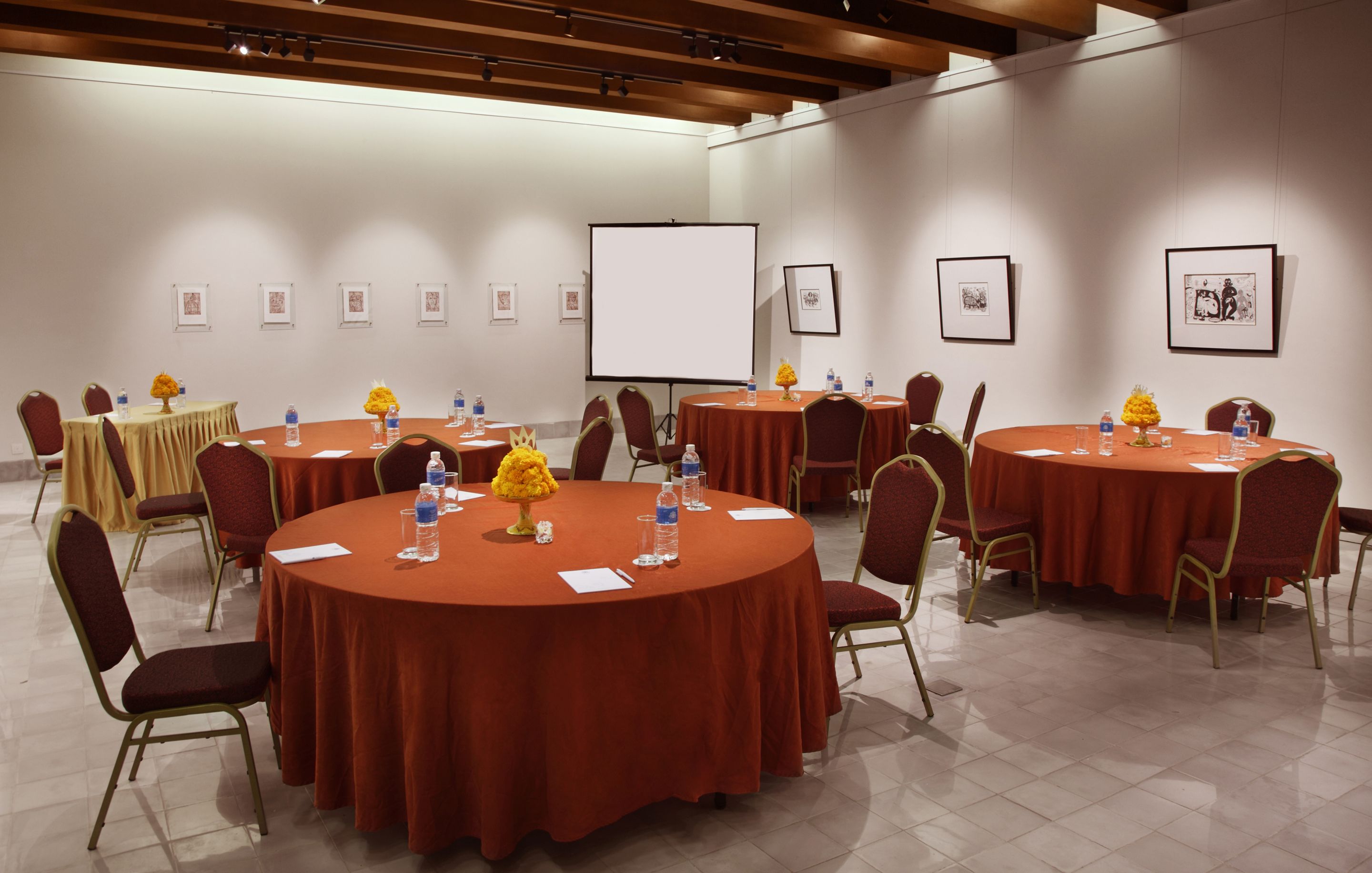 Un salón de conferencias con varias mesas redondas, sillas y una pantalla para proyector.