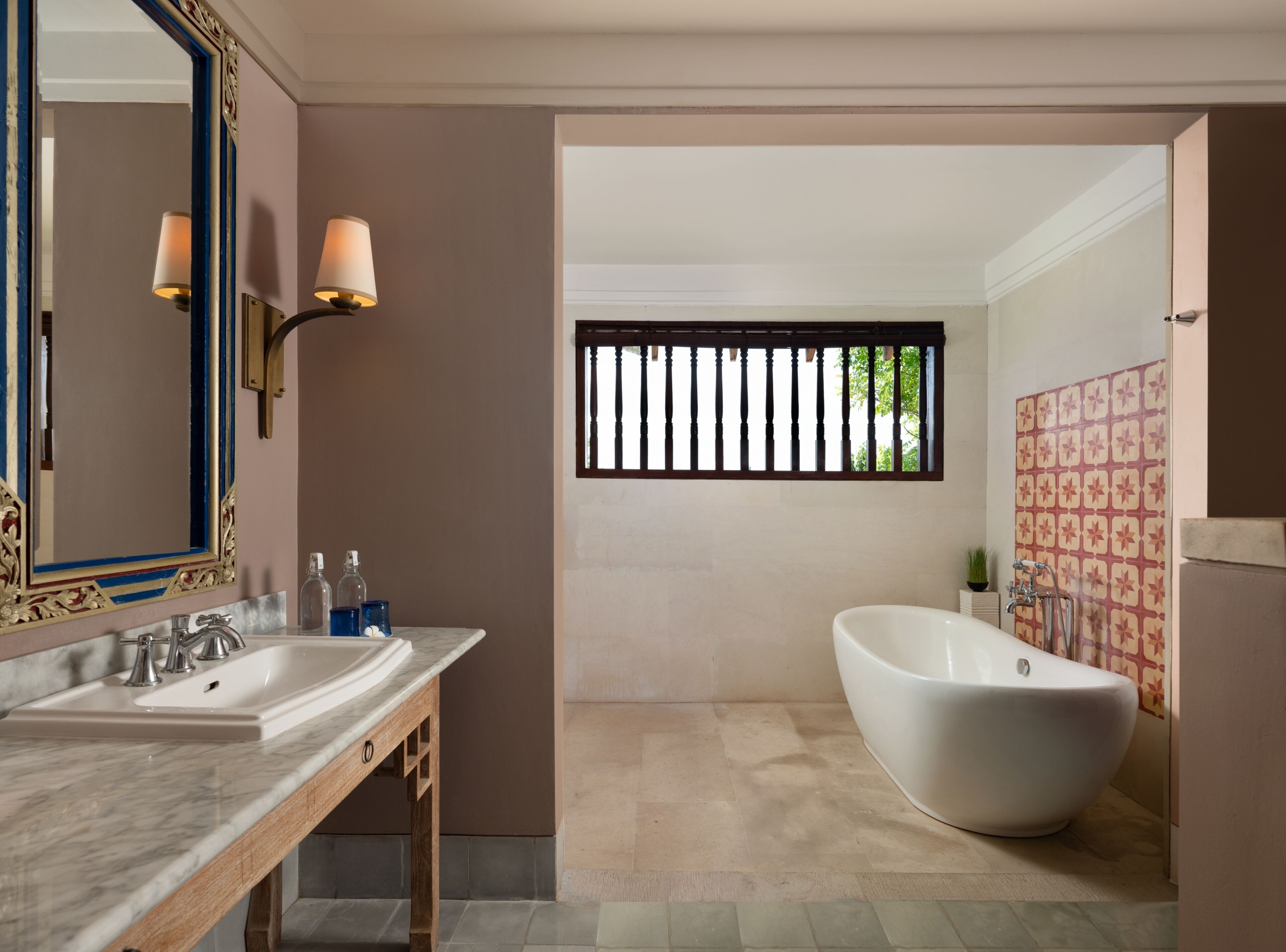 A bathroom with a freestanding bathtub, a large mirror with wall sconces, and a vanity with a marble countertop.
