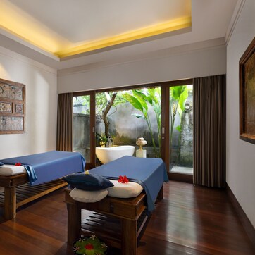 A room with two massage tables, a large painting, and a view of greenery outside.
