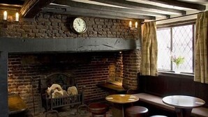 Een rustieke kamer met een stenen open haard, een ronde houten tafel en twee krukken.