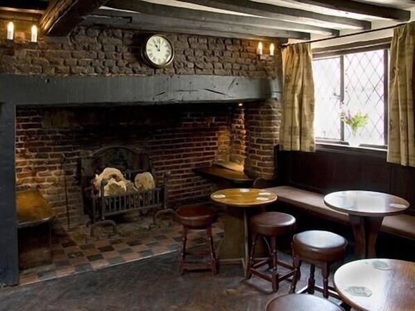 A rustic room with a stone fireplace, a round wooden table, and two stools. - The Brocket Arms (Welwyn)