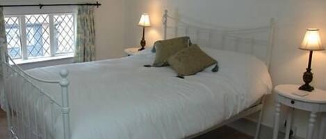 A bedroom with a large bed, two bedside tables with lamps, a window with curtains, and a white bed frame.