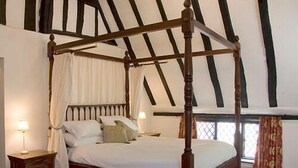 Een hemelbed met een baldakijn, een nachtkastje en een raam met gordijnen.