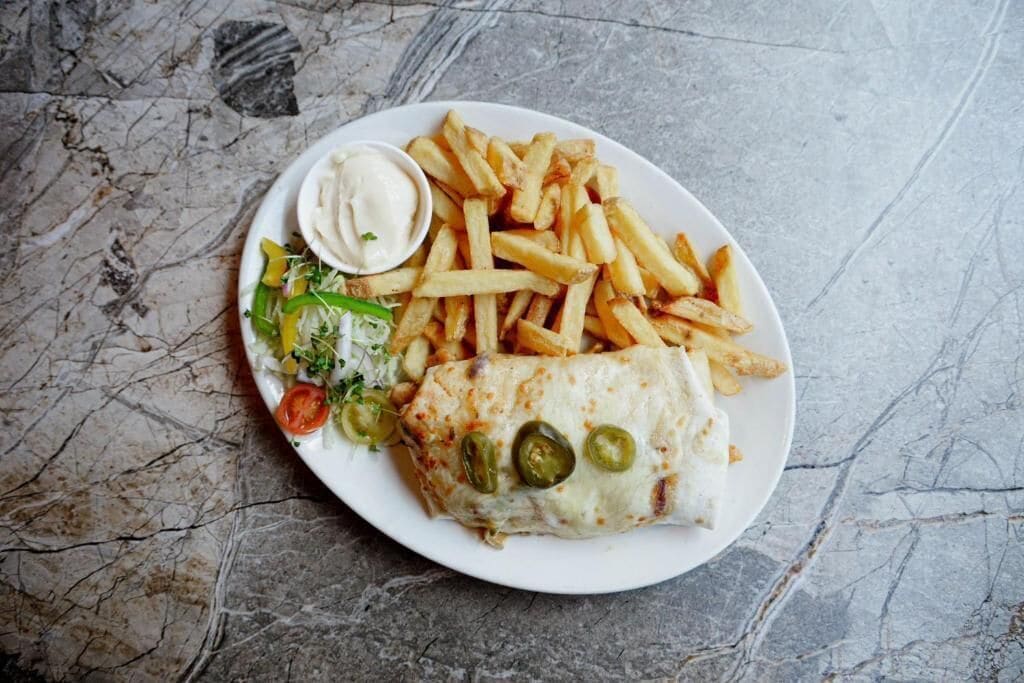 A plate with a wrap, fries, and a side salad.