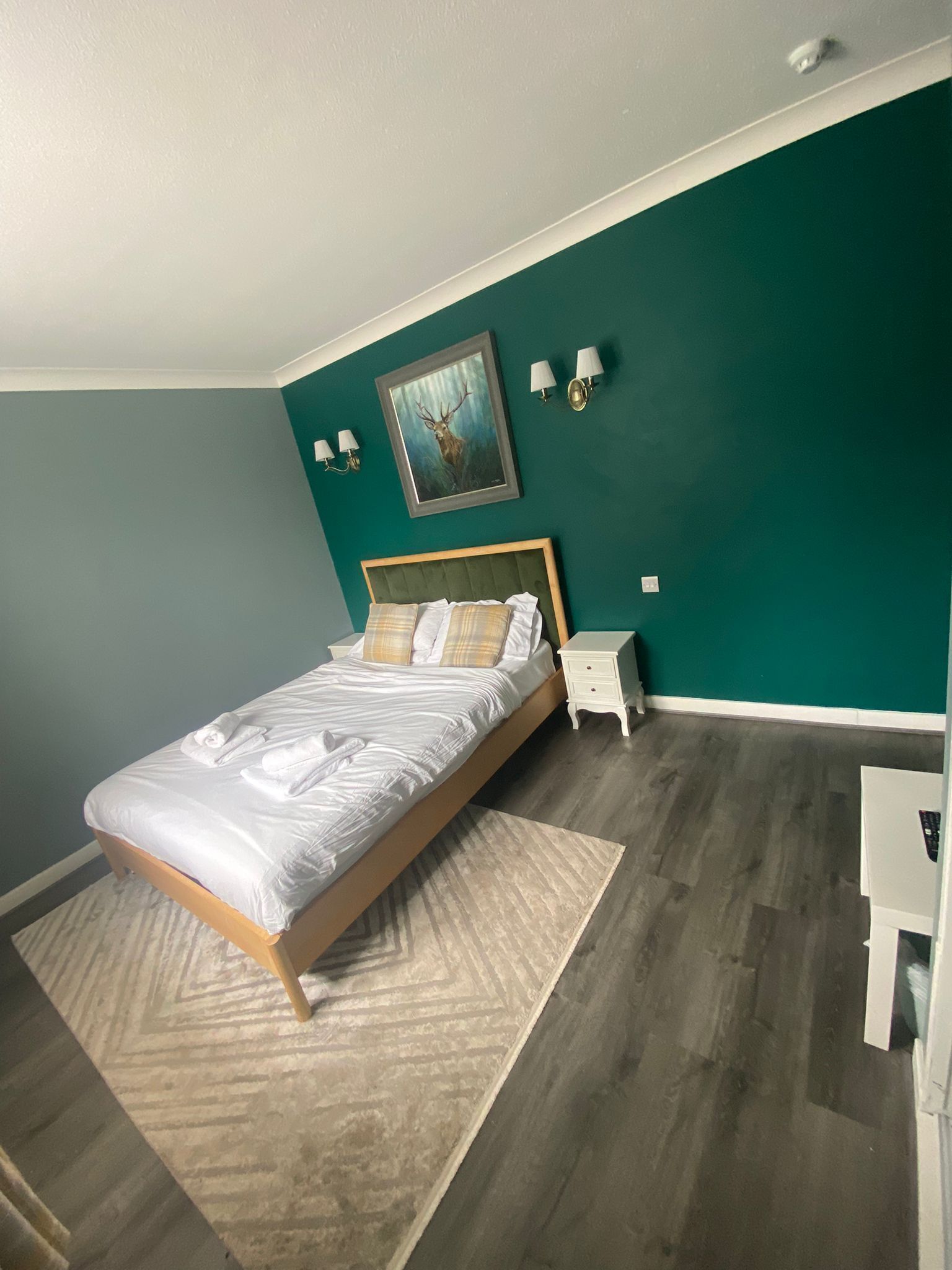 A bedroom with a bed, a nightstand, a lamp, and a painting on the wall.