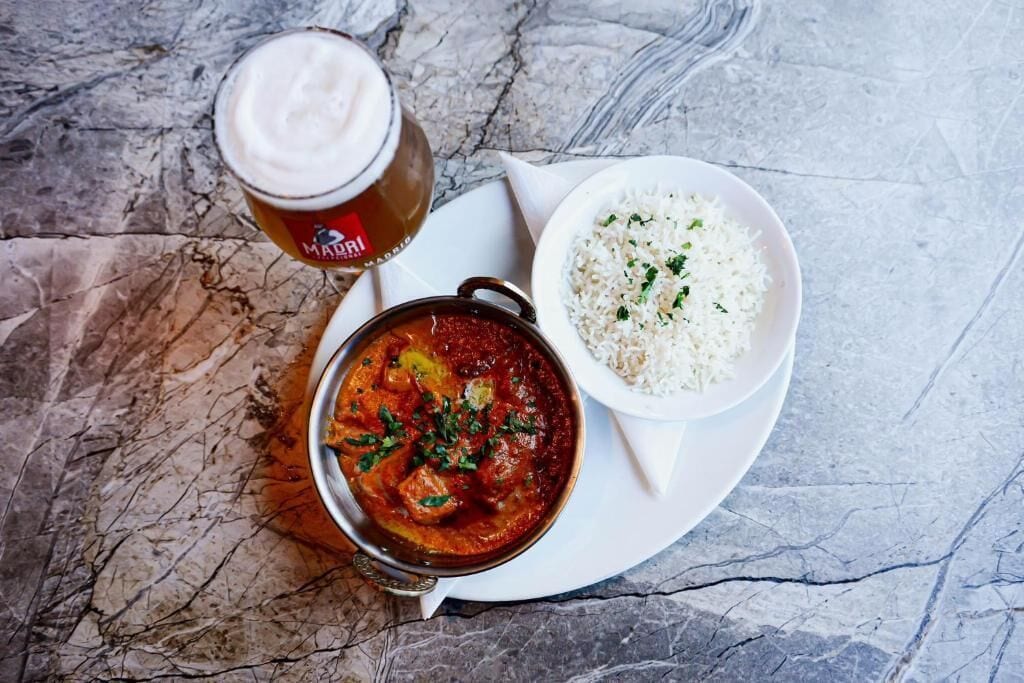 A meal consisting of a bowl of rice, a bowl of curry, and a glass of beer on a marble table.