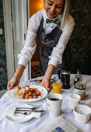 A person serving a meal with a plate of food, a coffee pot, a glass of orange juice, and a newspaper on a table. - Ralph's (Craigavon)