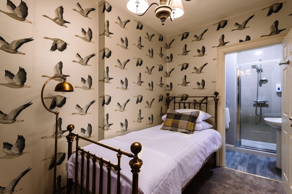 A bedroom with a bed, a nightstand, a lamp, and a shower area.